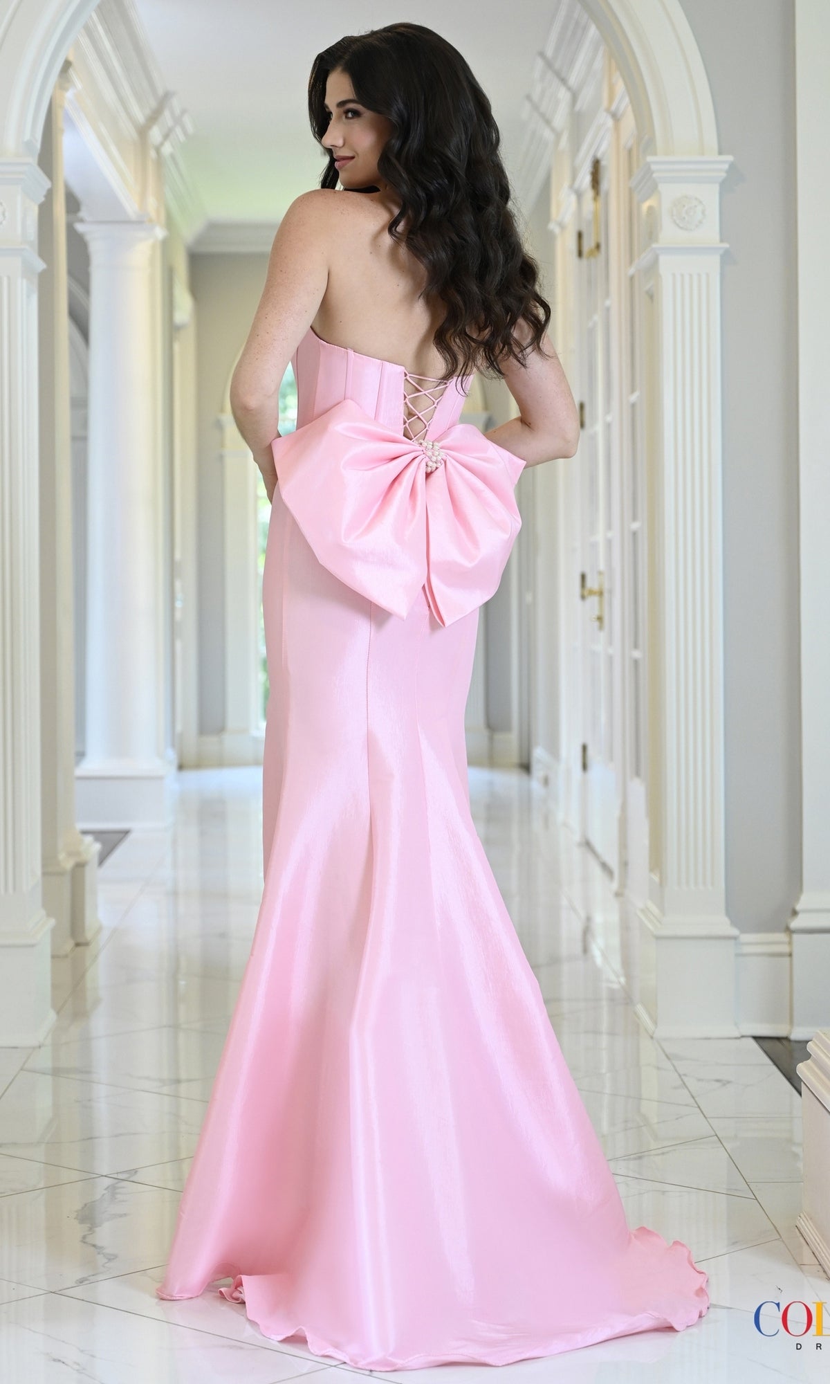 Colors Dress 4195 is a strapless, floor-length pink mermaid prom dress with a lace-up back, pearl trim, and a large bow at the waist.